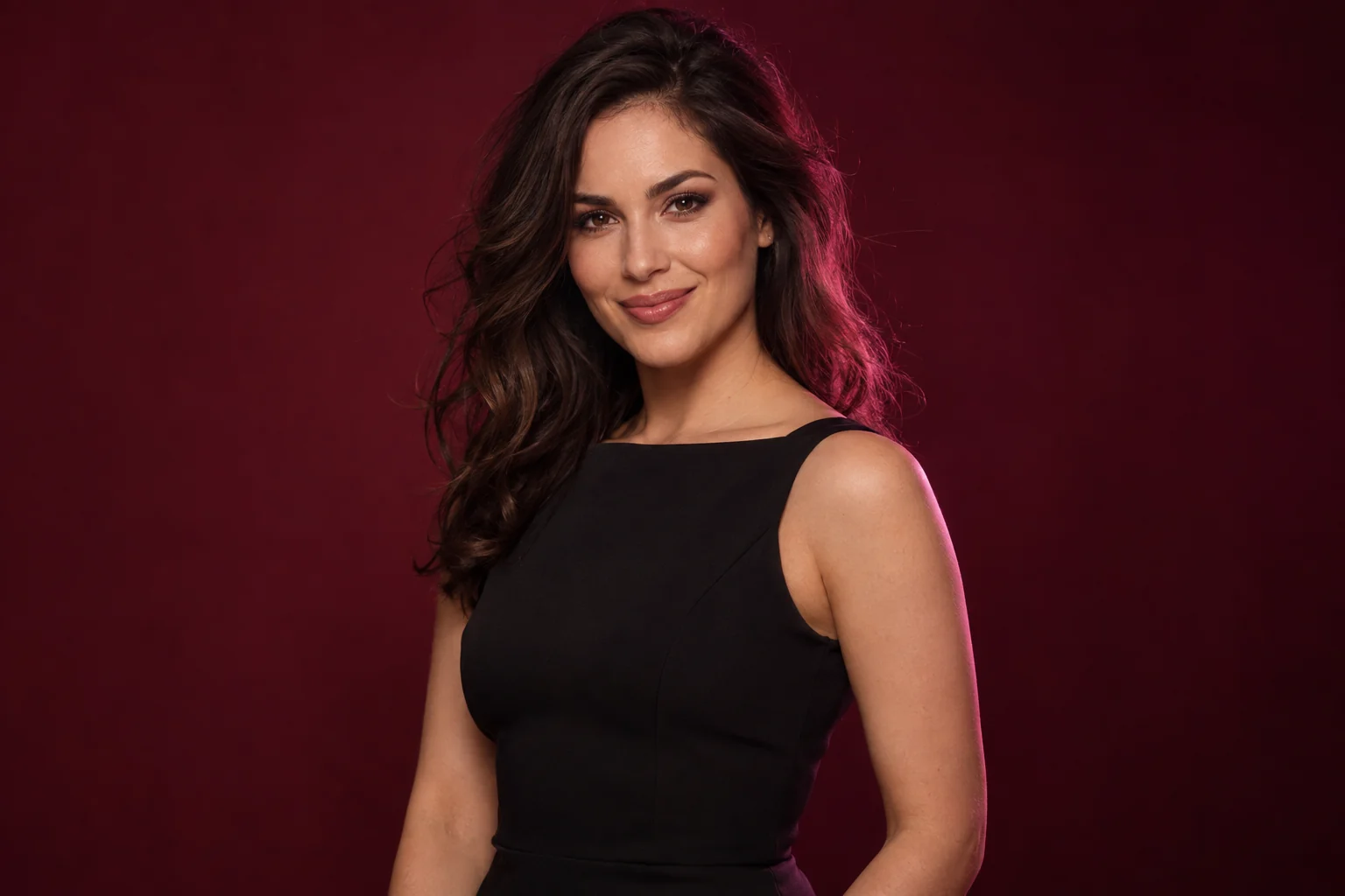 An adult brunette woman in a black evening dress under rose lighting